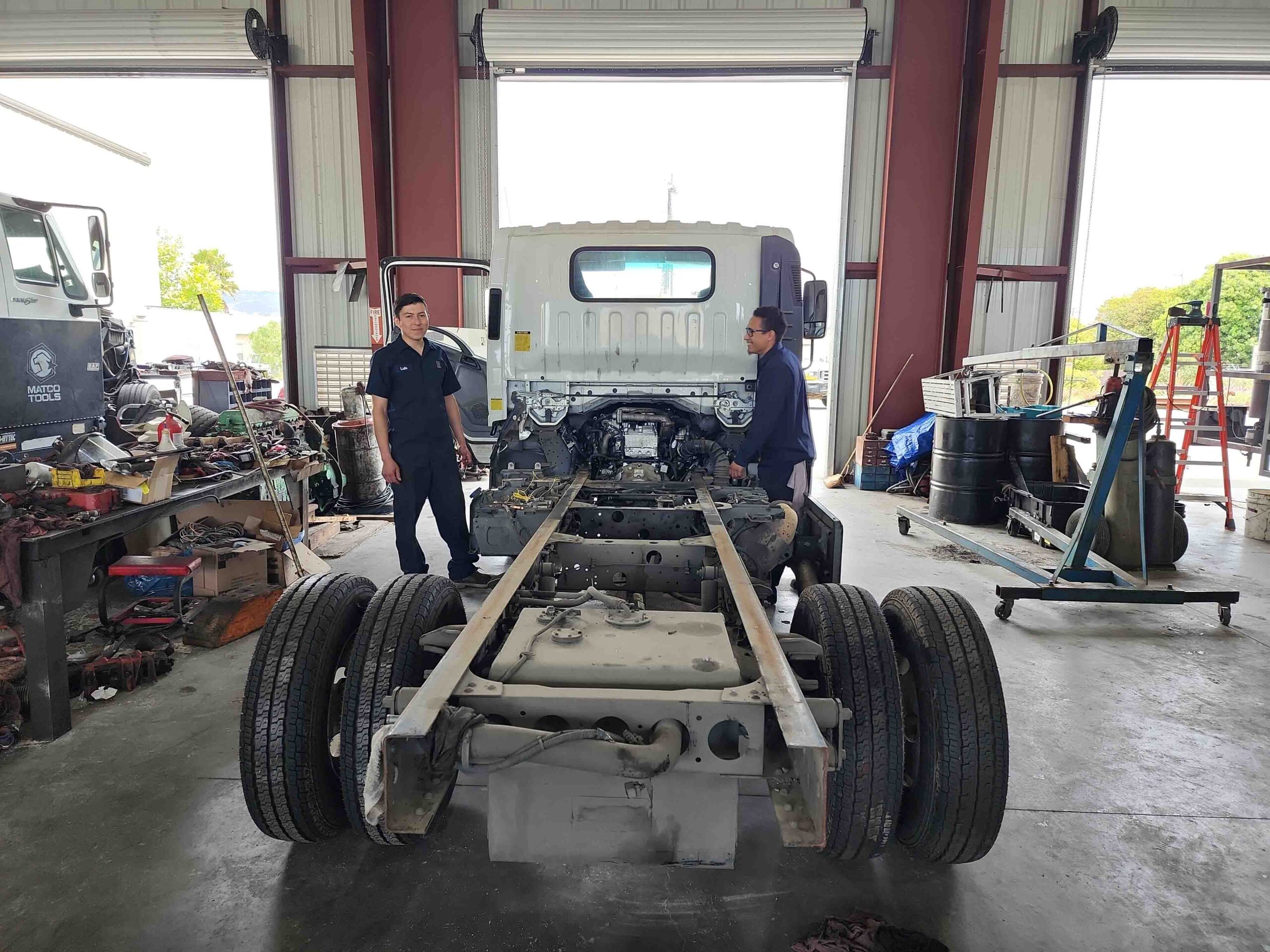 Watsonville Diesel Shop - two of the employees pose for a picture, next to one of the commercial trucks they're working on. These guys can obviously take the whole truck apart and put it back together if they want to, which seems to be what they're doing!