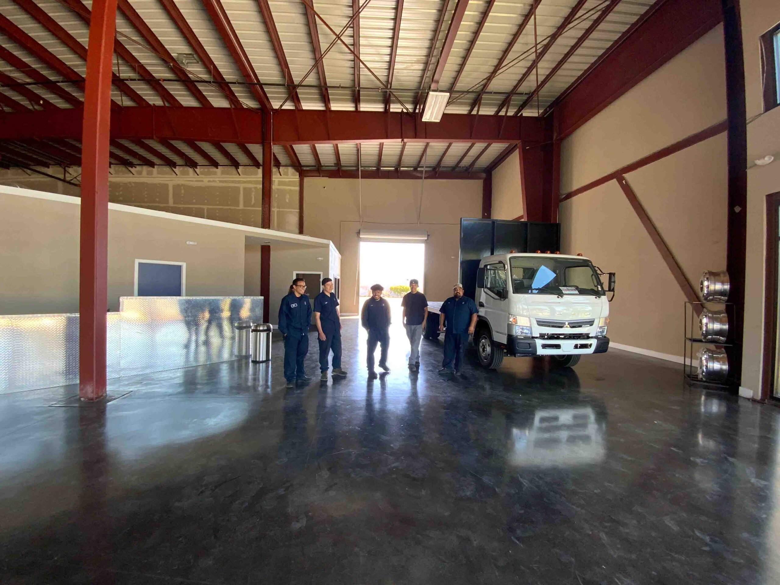 Watsonville Diesel Main Entryway - A brand new Isuzu truck sits on display in the lobby. A, "FOR SALE," sign rests on the dash. The guys from the shop are posing for a picture, smiling.