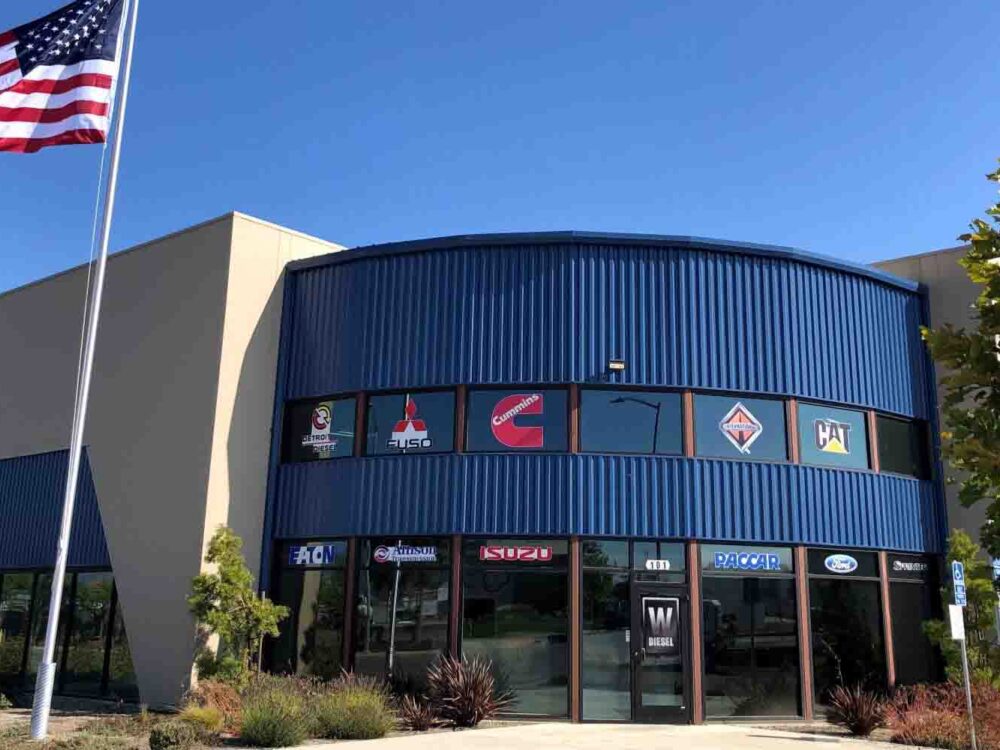 Watsonville Diesel headquarters building - front view. An American flag blows in the wind. The building is blue and tan. It's new construction.