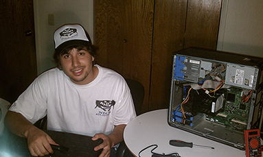 Nicholas Head, CEO of Do It Right Computers, Inc. fixing a computer. A voltmeter and screwdriver sit on the table next to an open chassis.